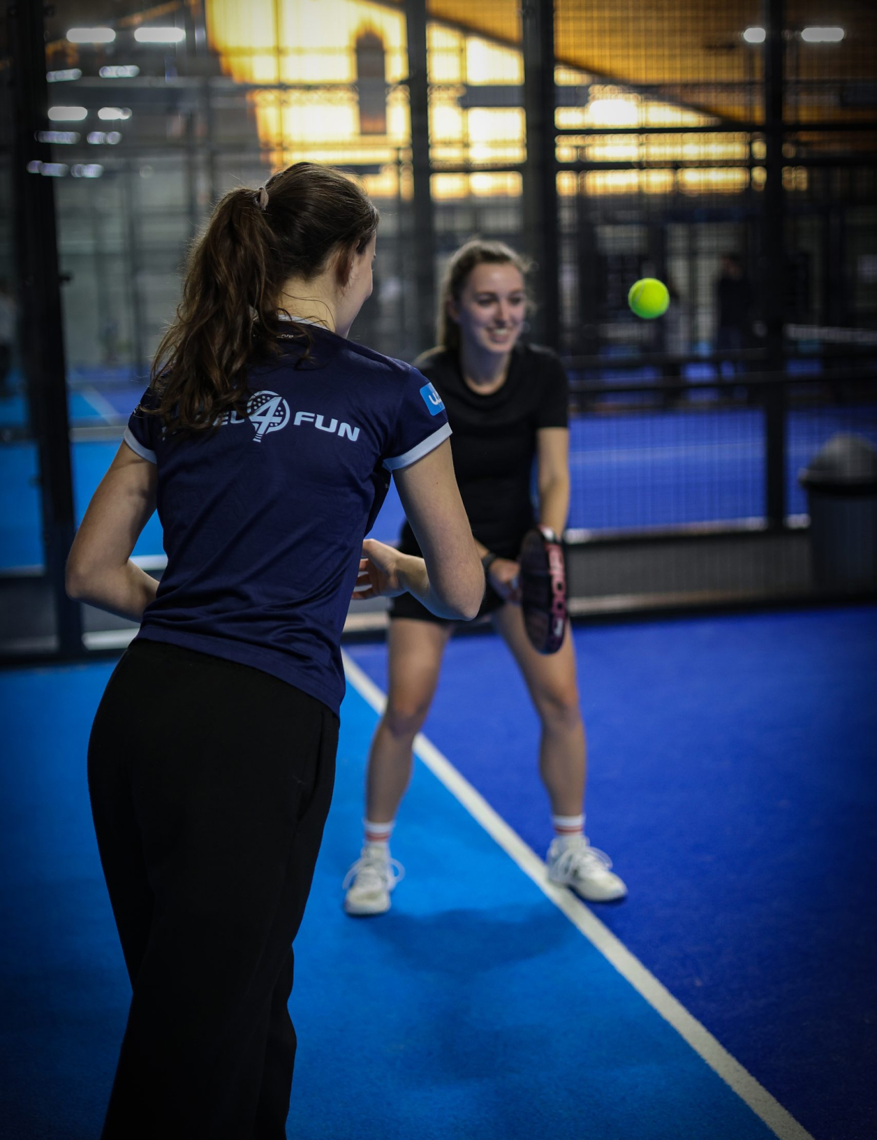 Am Padel Court steht ein Griller mit Grillgut, in der Zange ein Padel Ball.